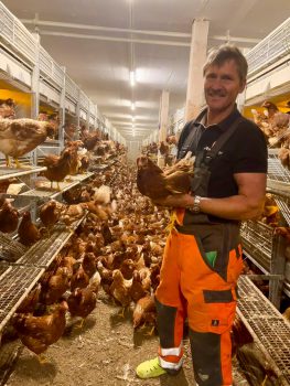 Peter Loibl im Hühnerstall mit einem Huhn in der Hand